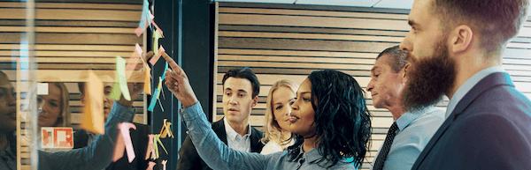 woman using post-its at wall surrounded by colleagues