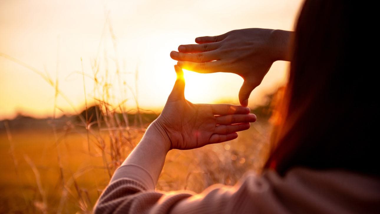 woman standing in a field holding her hands around the sun